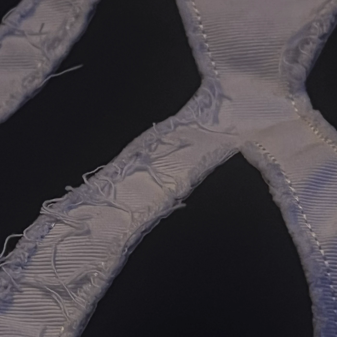 Macro detail of the embroidered IN patch — visible stitching, frayed thread edges and woven texture.
